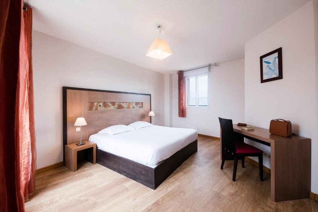 Ein Hotelzimmer mit Bett, Nachttisch, Lampe, Schreibtisch, Stuhl und einem Bild an der Wand.