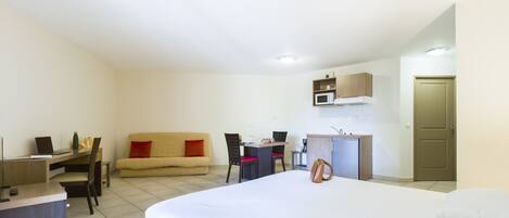 Una camera d'albergo con un letto, una scrivania, un divano, un tavolo da pranzo e angolo cottura.