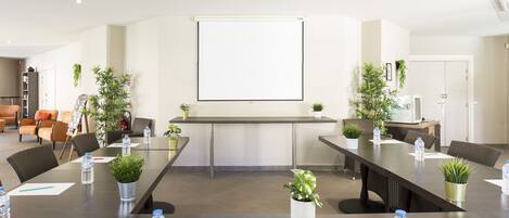 Un salón de conferencias con una larga mesa, sillas, botellas de agua y plantas en macetas.
