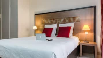 A neatly made bed with a laptop and remote control, a wooden headboard with a leaf pattern, and two bedside lamps.