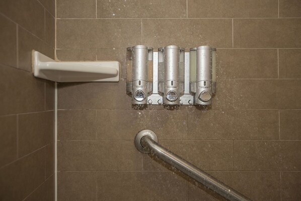 Un baño con zona de ducha, secamanos y dispensador de jabón de manos fijado a la pared.