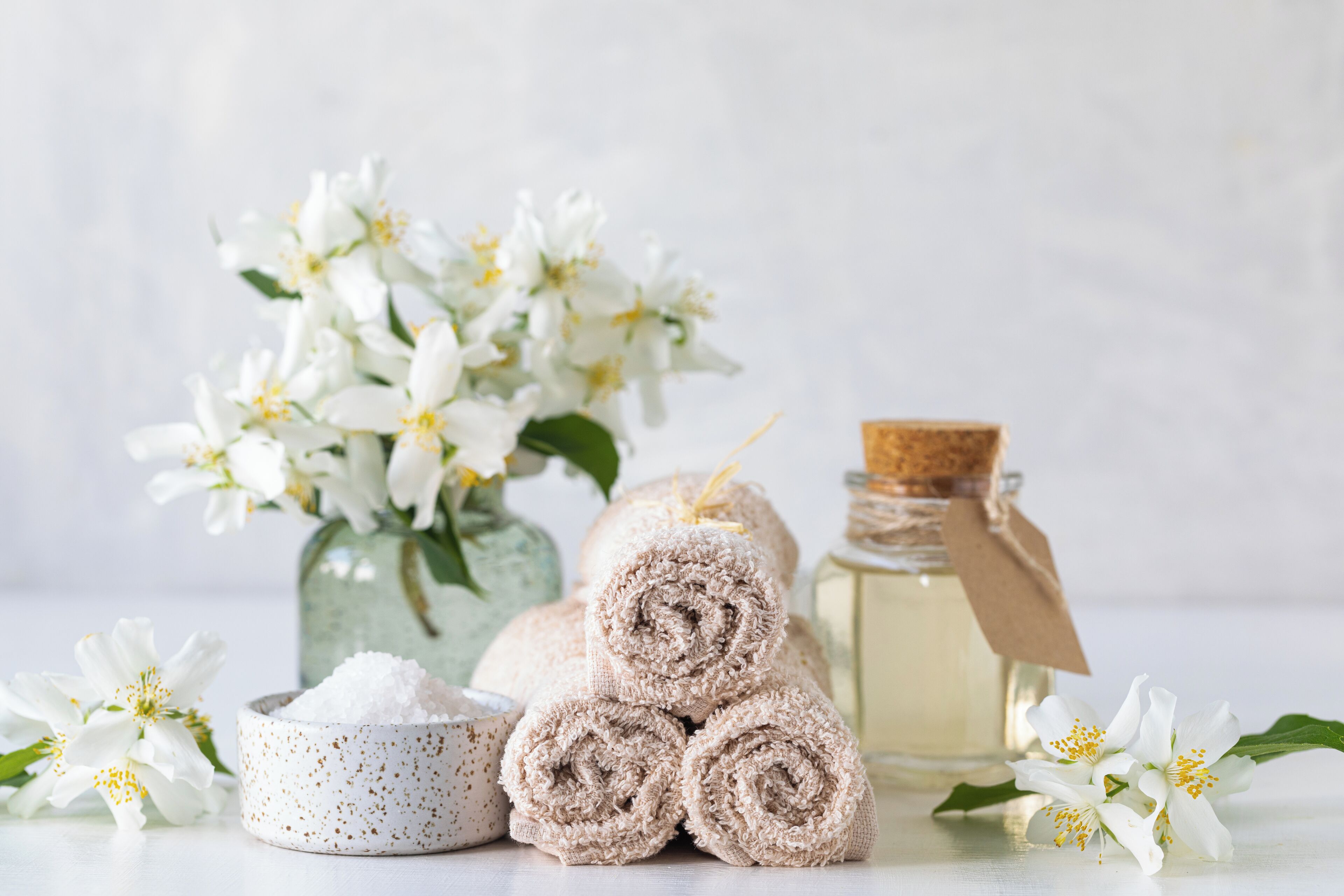 A spa setting with rolled towels, a jar of oil, and white flowers.