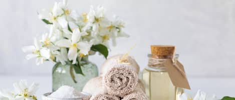 Een wellness omgeving met opgerolde handdoeken, een oliemeter en witte bloemen.