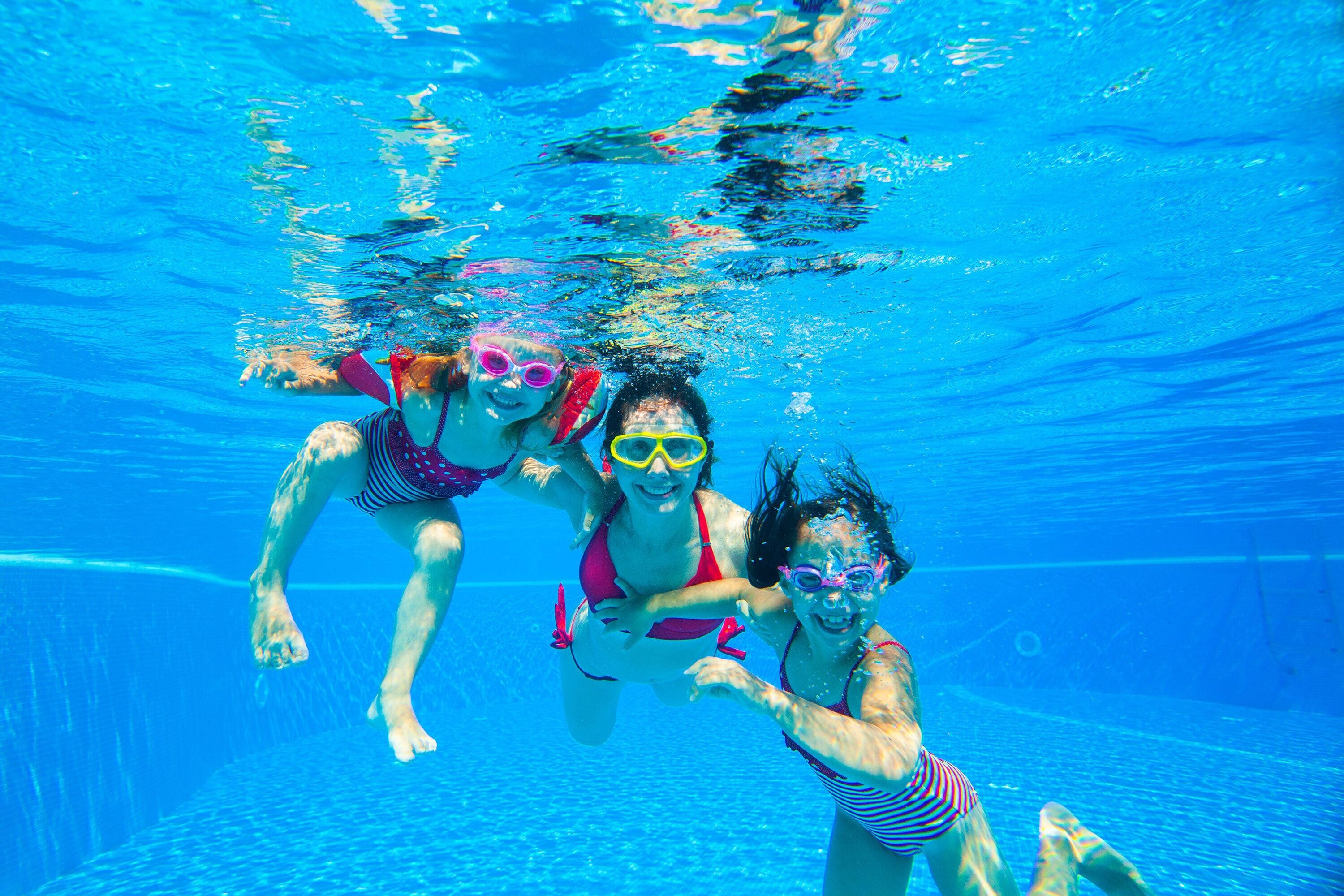 An underwater view of three people swimming in a pool.