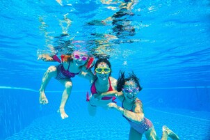 Vista subaquática de três pessoas nadando em uma piscina.