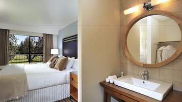 A hotel room with a large bed, a bathroom with a round mirror, and a view of the outdoors.