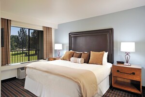 A hotel room with a large bed, two bedside tables, a window with curtains, and a view of a golf course.
