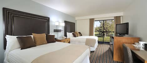 A hotel room with two beds, a desk, a television, and a balcony with a view.