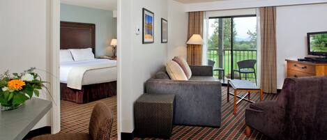 Quarto de hotel com cama, sofá, escrivaninha e televisão.