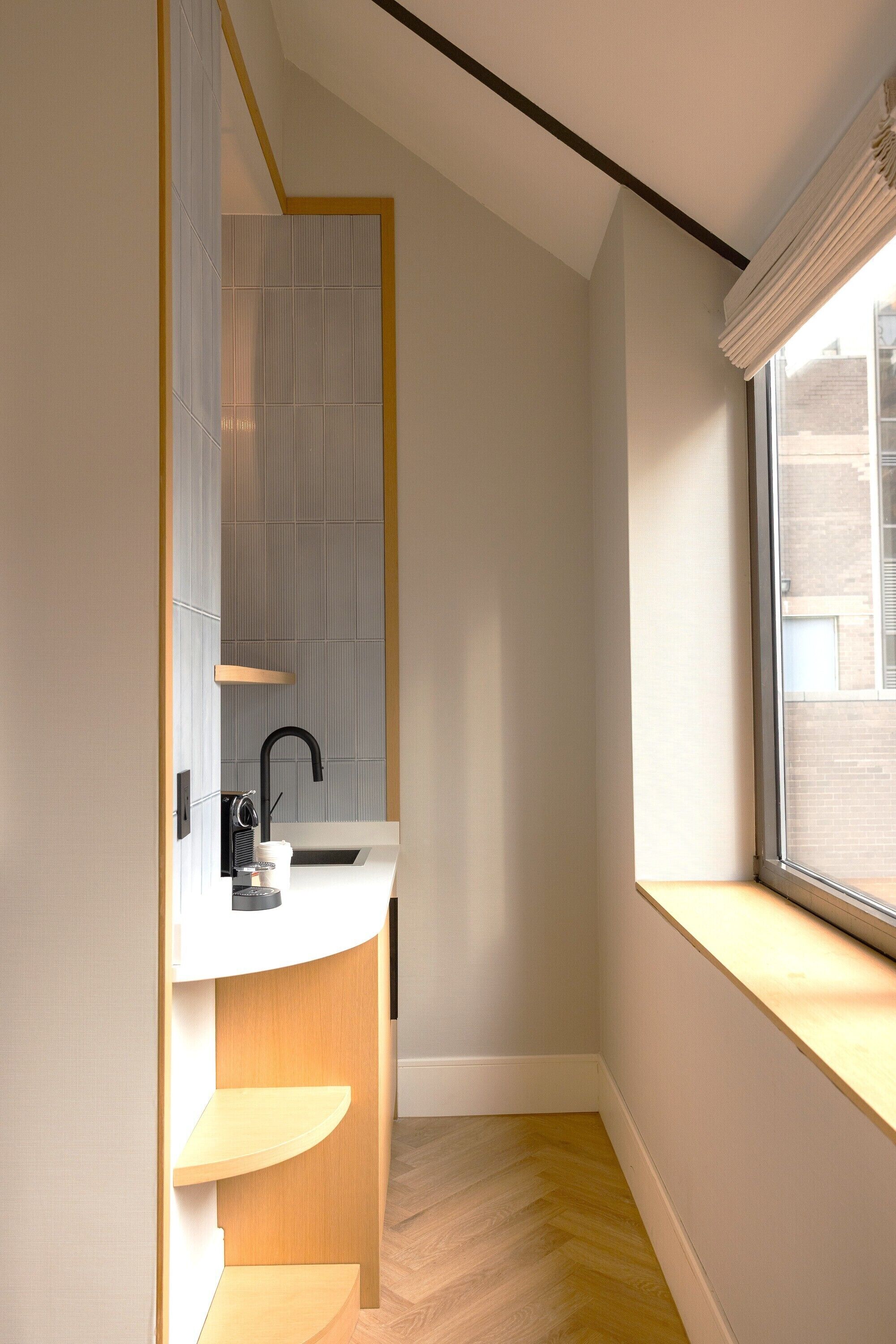 A modern bathroom with a white sink, black faucet, and a window with a white blind.