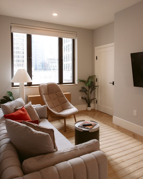 Un salon moderne avec un canapé, un fauteuil, une lampe et une petite table sur laquelle repose un magazine.