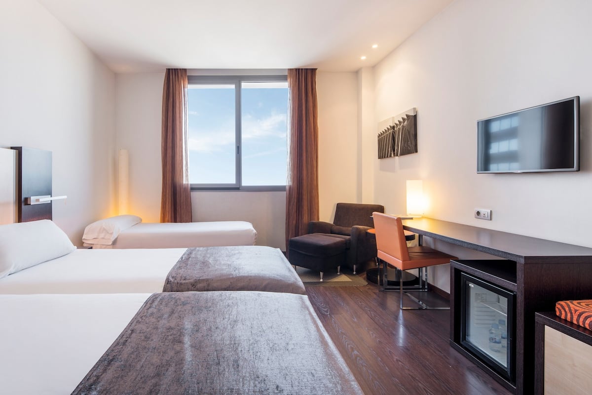 Une chambre d’hôtel avec deux lits, un bureau, une chaise, une télévision et une fenêtre avec des rideaux.