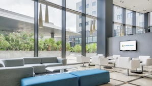 Un moderno vestíbulo de hotel con una zona de estar, una gran pantalla de televisión mostrando el nombre del hotel y vistas al jardín exterior.