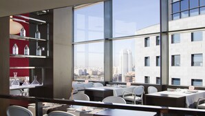 Un restaurante con mesas, sillas, ventanas amplias y vistas a la ciudad.