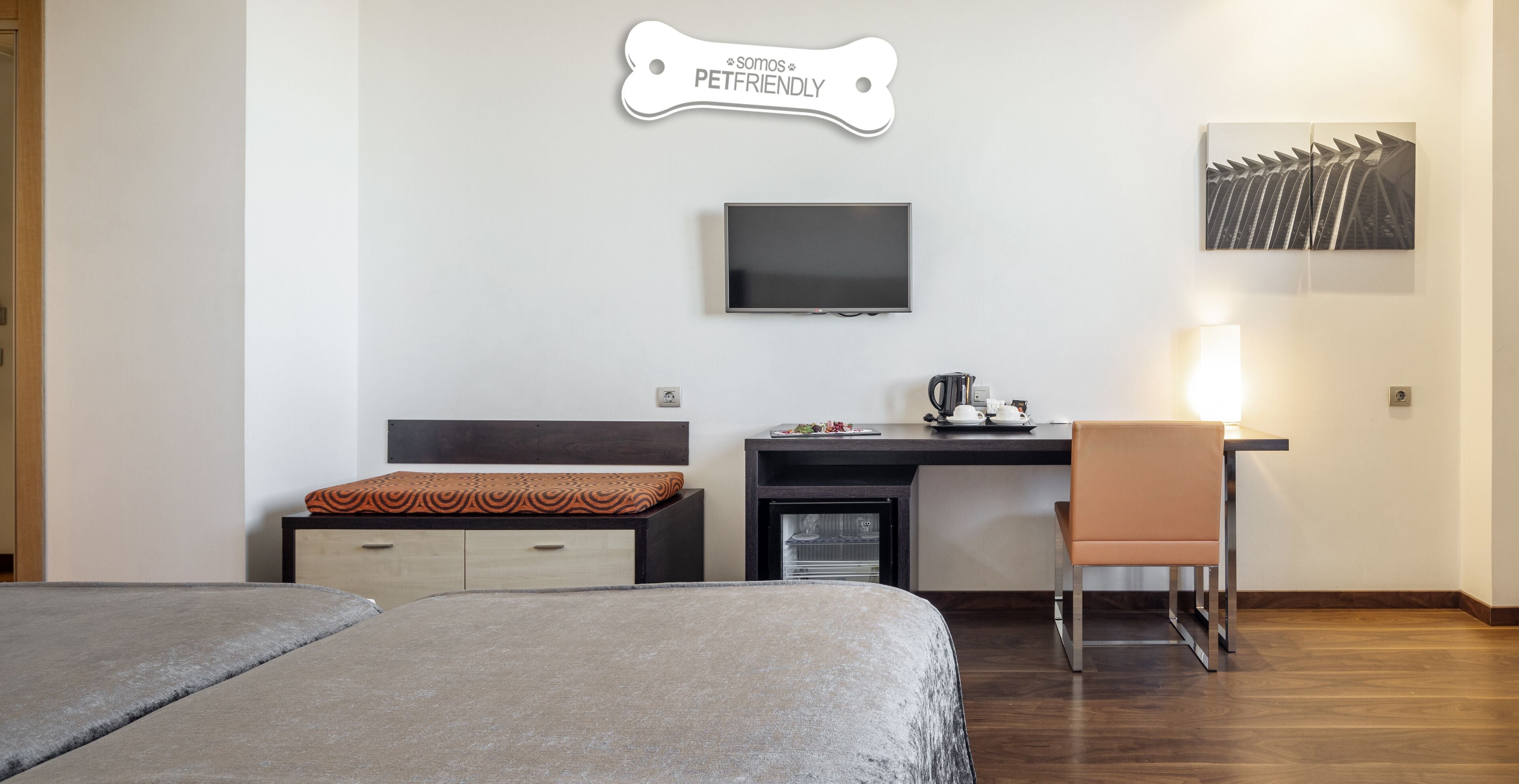 Una habitación de hotel con dos camas, un escritorio con una silla, un televisor y un letrero en la pared que dice "Somos PETFRIENDLY".