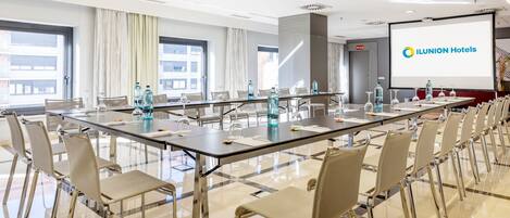 A conference room with a long table, chairs, and a projector screen displaying the Ilunion Hotels logo.