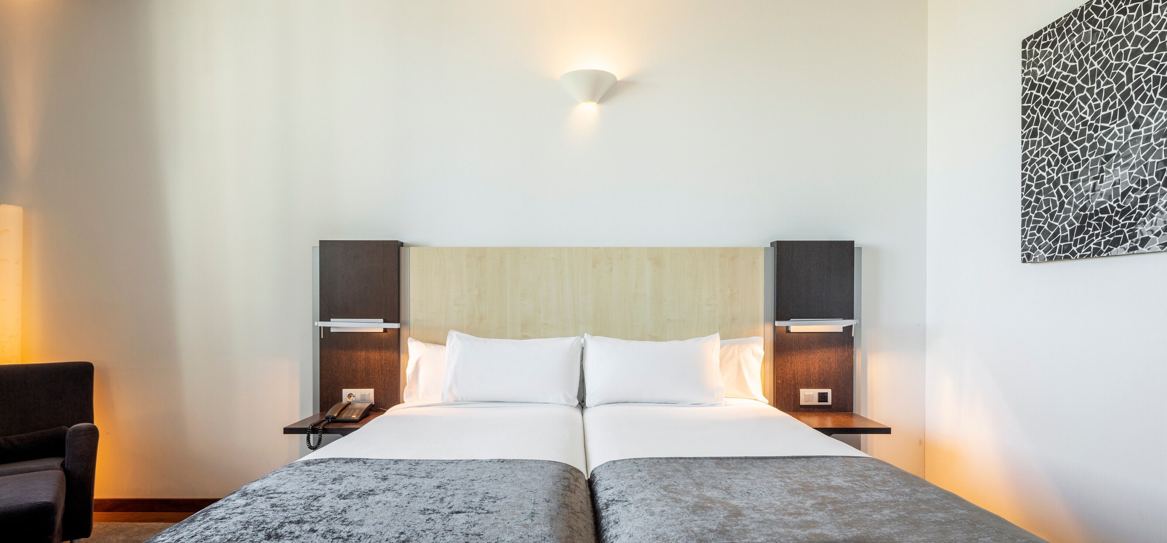 Una cama doble con cabecera de madera, mesitas de noche con lámparas, y una lámpara fijada a la pared.