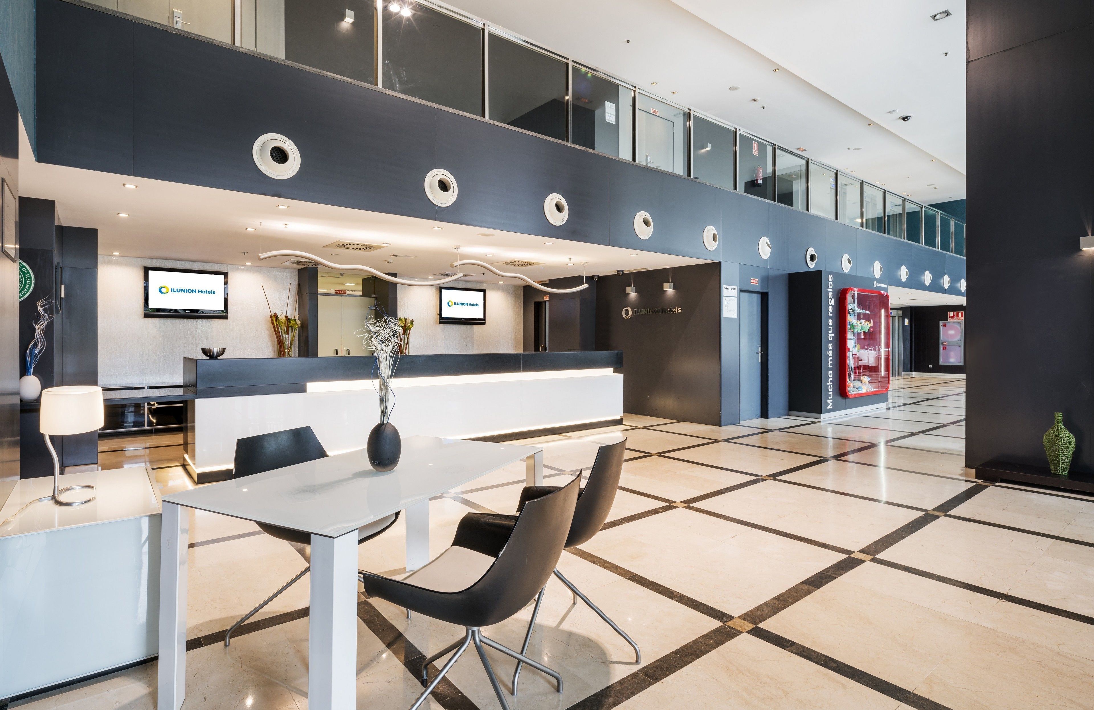 Una moderna hall d'albergo con reception, area relax e un grande schermo digitale che mostra il nome dell'hotel.
