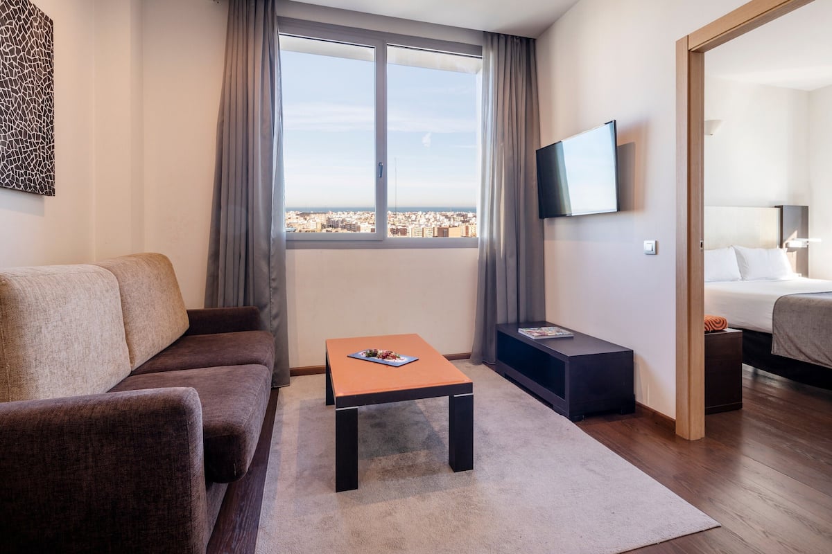 Une chambre d’hôtel moderne avec un canapé, une petite table, une télévision et un lit.