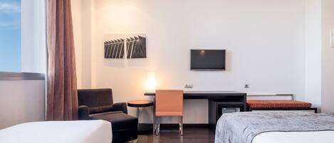 A hotel room with a bed, a desk with a chair, a TV, and artwork on the wall.