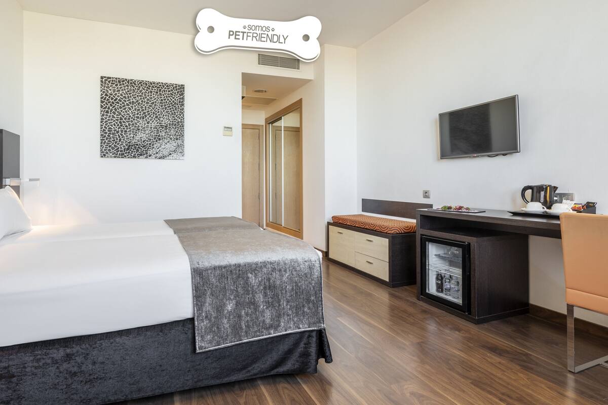 Une chambre d’hôtel moderne équipée d’un lit, d’un bureau, d’une télévision et d’un petit réfrigérateur.