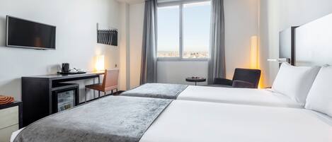 A hotel room with two beds, a desk, a TV, and a window with a city view.