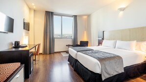 Habitación de hotel con una cama grande, un escritorio con una silla, un televisor y vistas a la ciudad a través de la ventana.