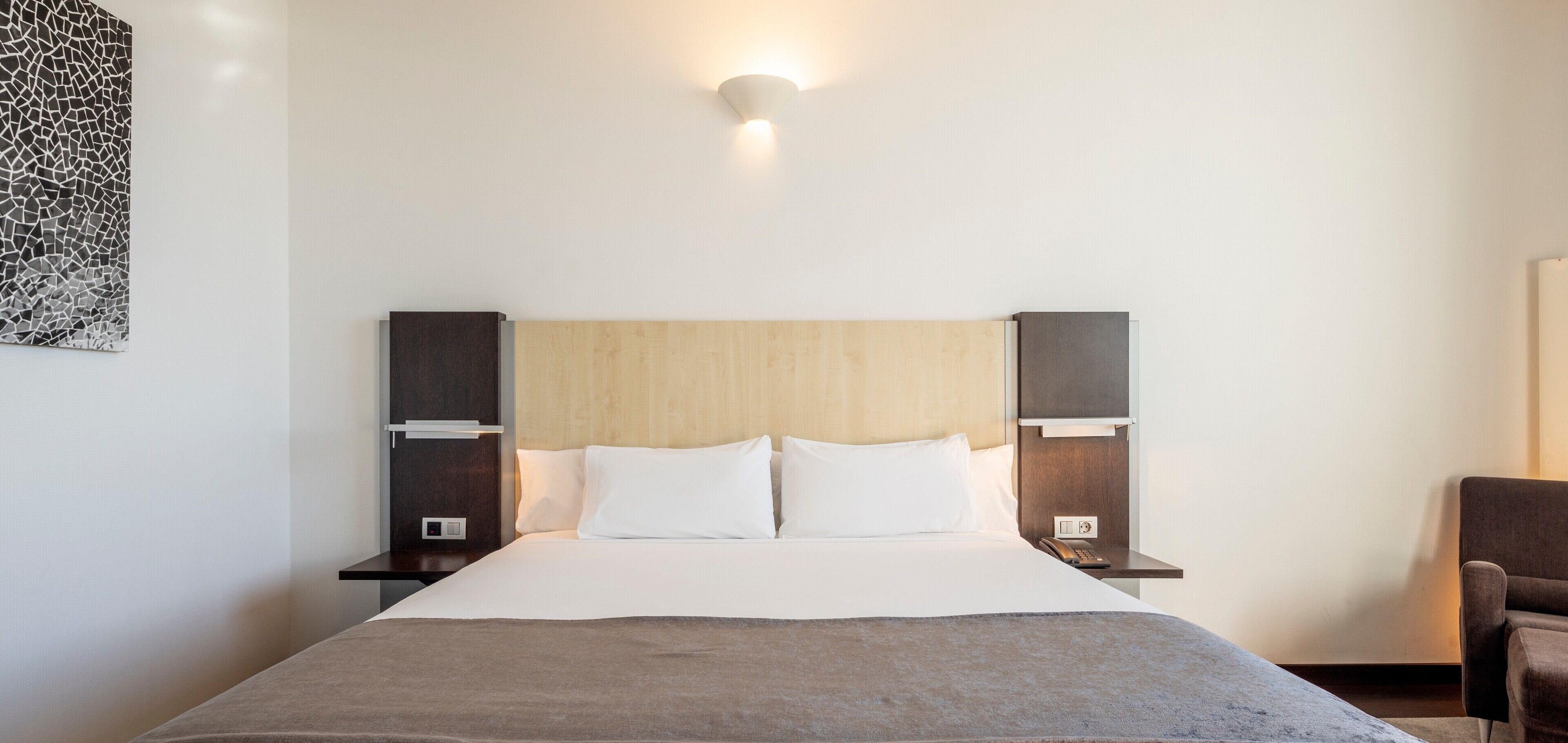 Habitación de hotel con una cama grande, dos mesitas de noche, una lámpara de pared y una obra de arte abstracta moderna.