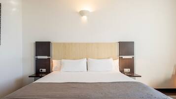 Habitación de hotel con una cama grande, dos mesitas de noche, una lámpara de pared y una obra de arte abstracta moderna.