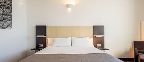 Habitación de hotel con una cama grande, dos mesitas de noche, una lámpara de pared y una obra de arte abstracta moderna.