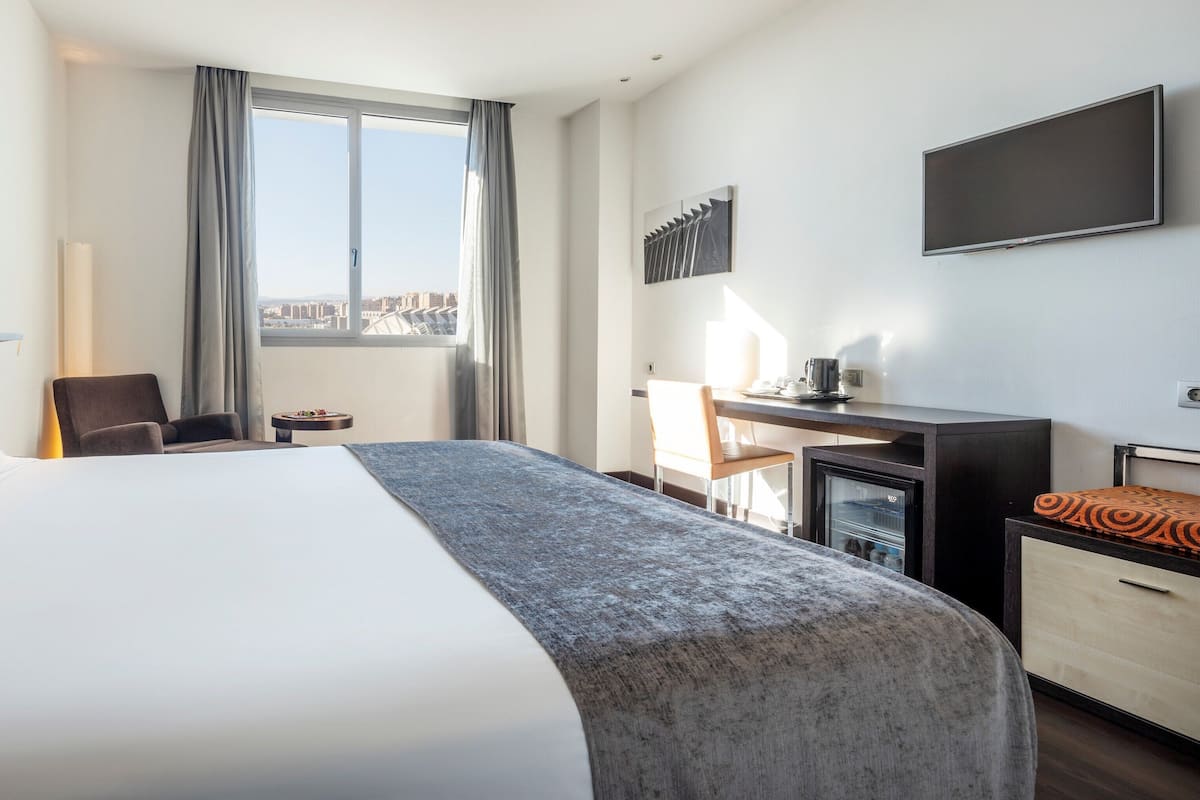 Une chambre d’hôtel avec un grand lit, un bureau, une chaise, une télévision et une vue sur la ville.