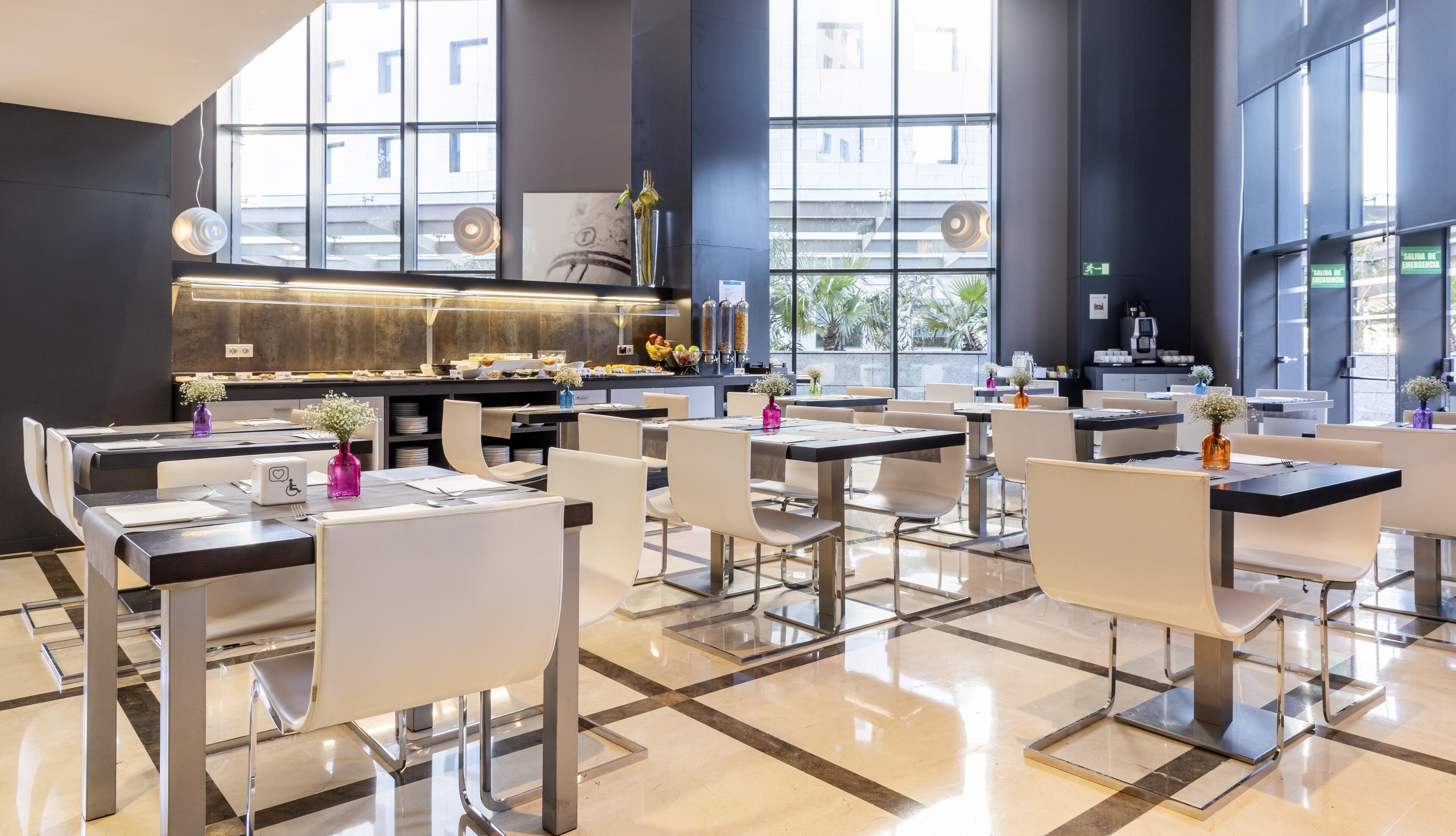 A modern restaurant with a high ceiling, large windows, and a central kitchen area.
