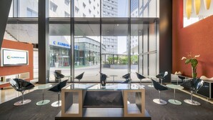 A modern hotel lobby with a glass partition, contemporary chairs, and a large window offering a view of the street and buildings outside. - Hotel ILUNION Aqua 3 (Valencia)