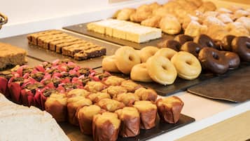 Variedad de productos horneados, como muffins, donas y pasteles, expuestos en una barra.