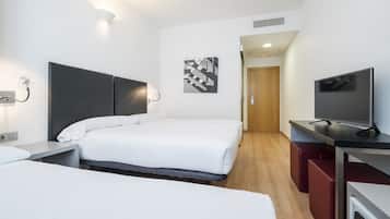 Habitación de hotel con cama, mesitas de noche, televisor, escritorio y puerta que da a un pasillo.