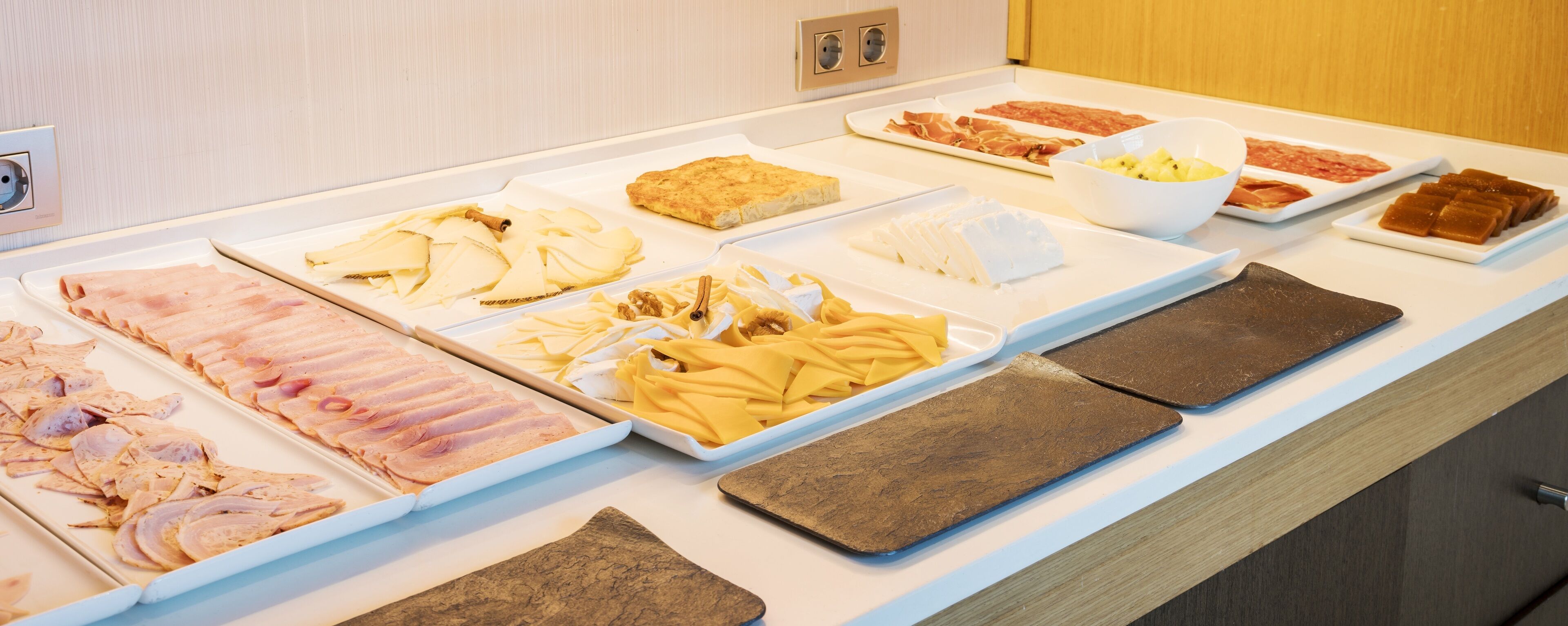 Un bufé con diversas opciones de comida, incluyendo carnes, quesos y frutas.