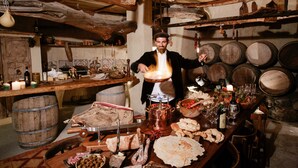 Una cocina rústica con barriles de madera, una olla de cobre y varios alimentos sobre la encimera.