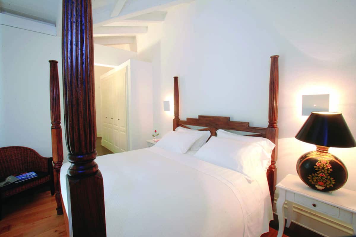 A neatly made bed with white linens, a wooden headboard, and a bedside table with a lamp.