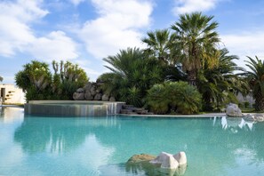 Una piscina cristalina con cascada, rodeada de palmeras y rocas.
