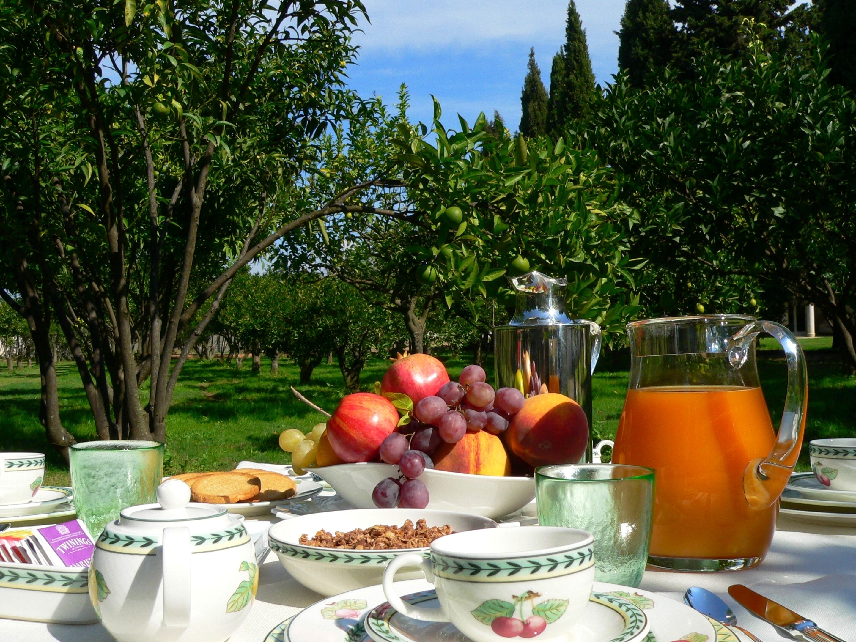 Colazione con frutta, una brocca di succo d'arancia e tazze da tè e caffè su un tavolo all'aperto.