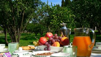 Colazione con frutta, una brocca di succo d'arancia e tazze da tè e caffè su un tavolo all'aperto.