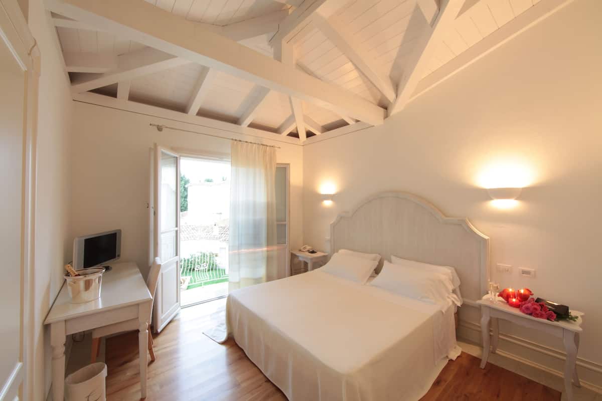 A bedroom with a bed, bedside tables, a desk with a computer, and a window with curtains.