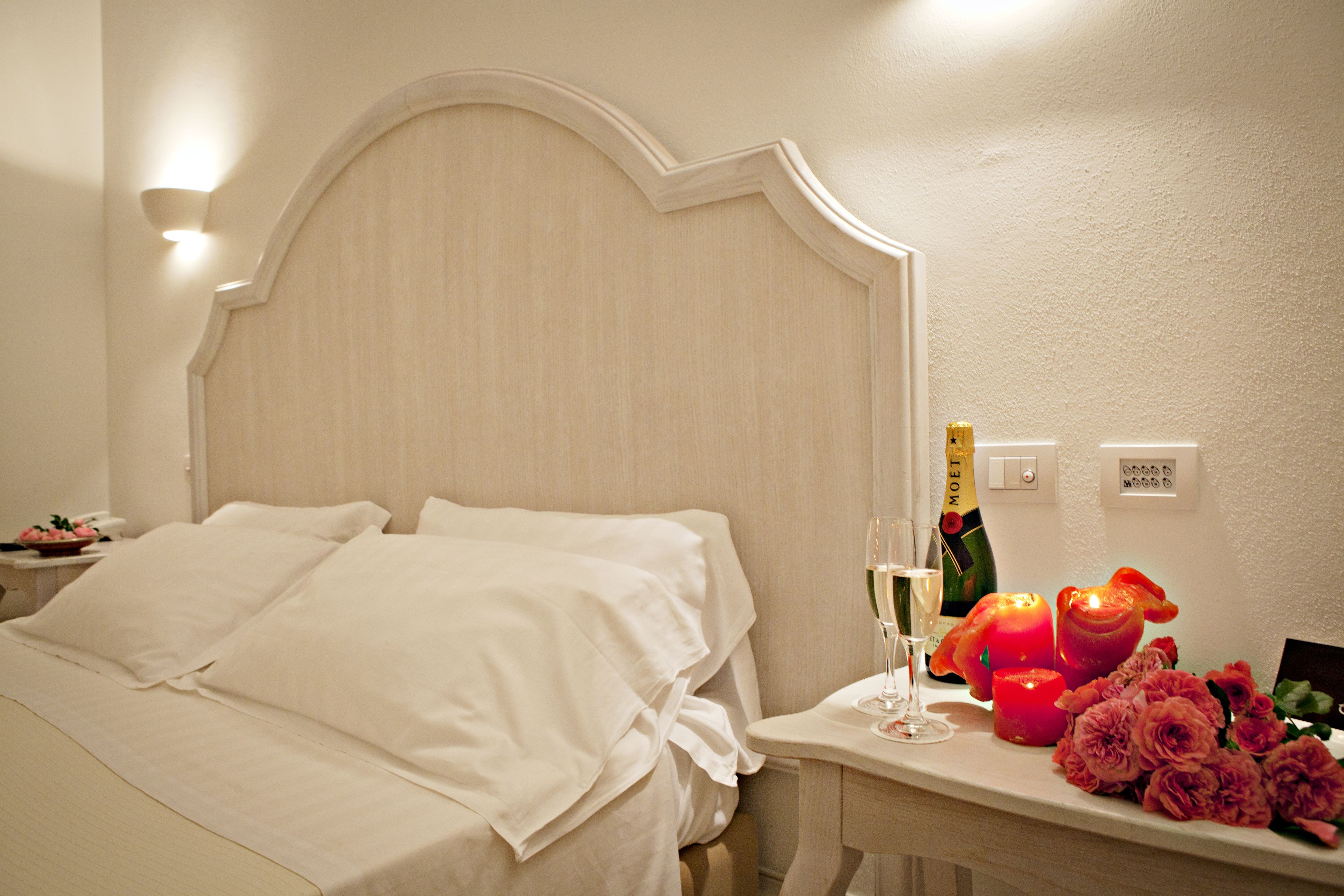 Una camera d'albergo con un letto, un comodino con una bottiglia di champagne, un bicchiere e delle candele.