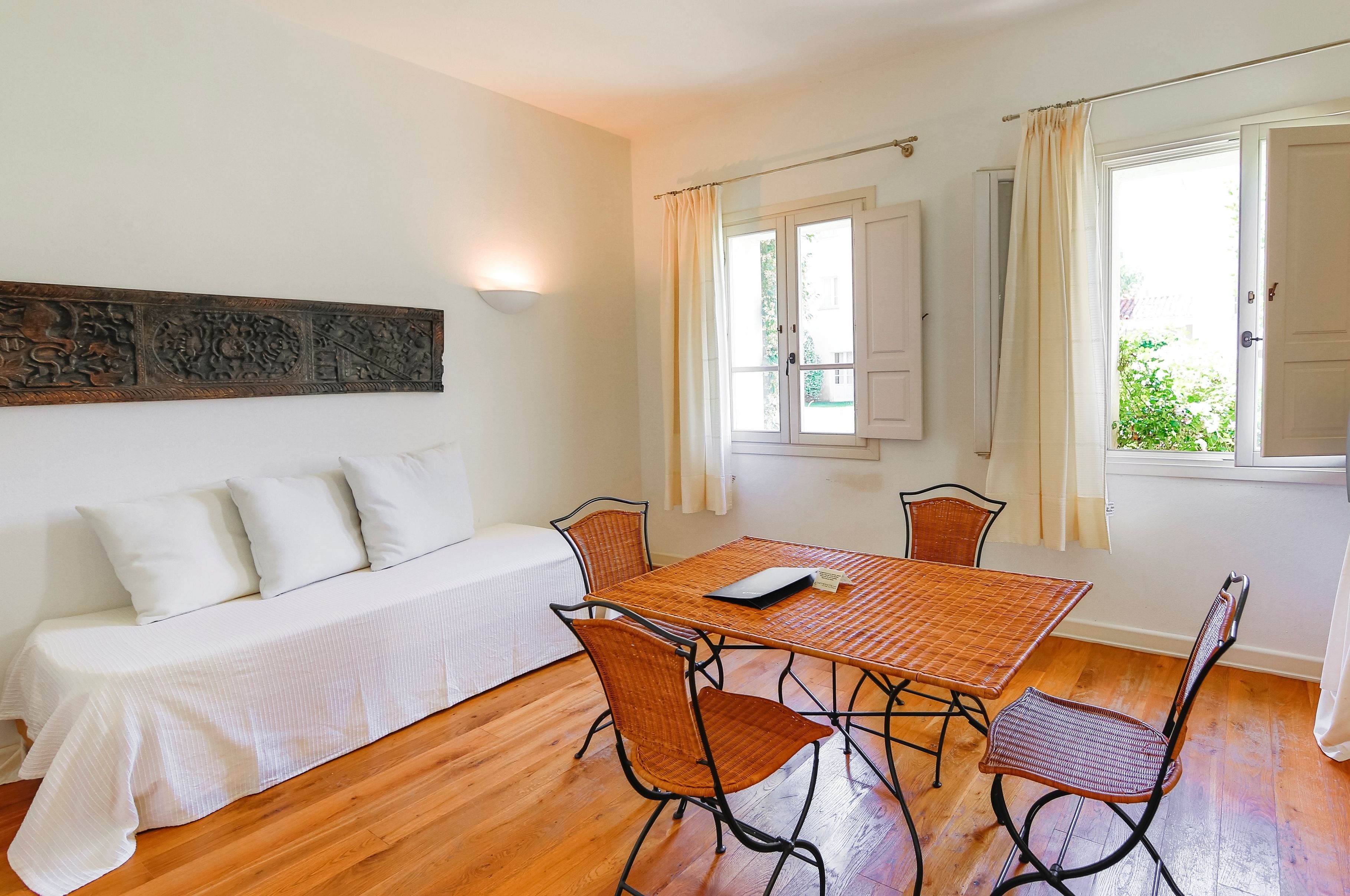 Una habitación con una cama, una mesa de comedor con sillas, una lámpara de pared y un ventanal con cortinas.