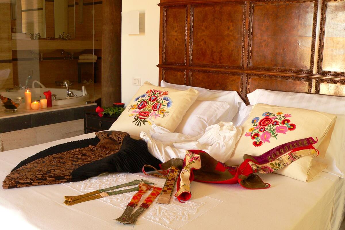 A neatly made bed with floral pillows, a wooden headboard, and a bedside table with candles.