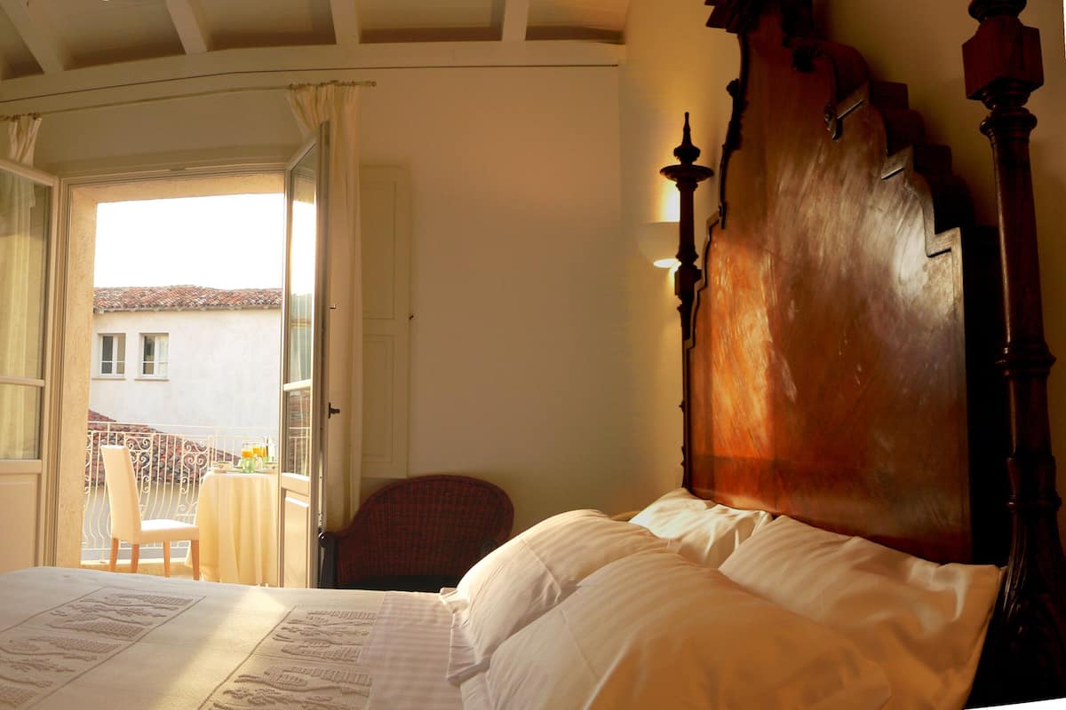 A bedroom with a large bed, a chair, and a table with a view of a building outside.