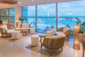 A modern lounge area with wicker furniture, white cushions, and large windows offering a view of the sea. - Serhs Natal Grand Hotel & Resort (Natal)