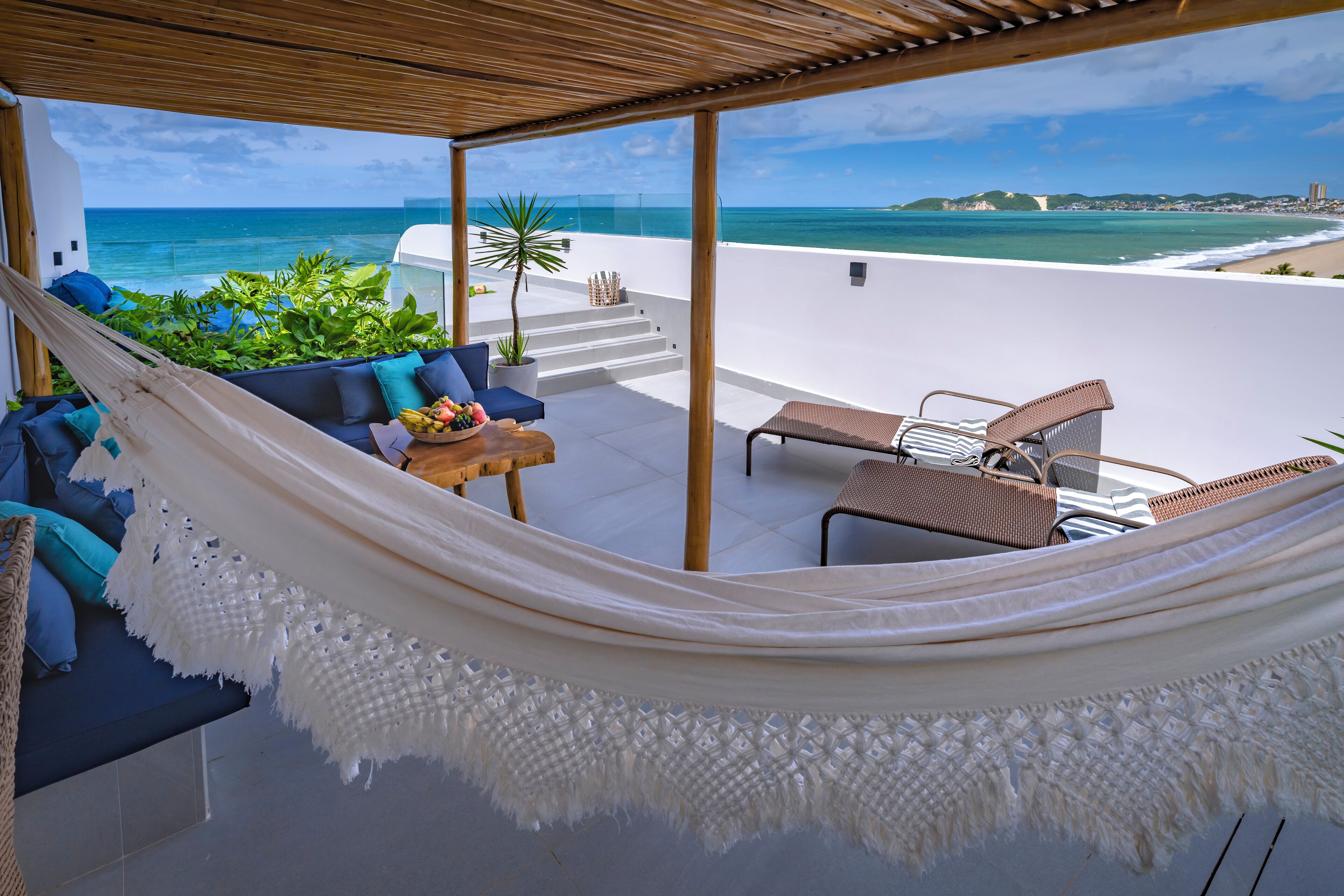 A hammock over a white sofa with a view of the ocean and a beach.