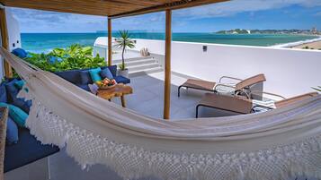 A hammock over a white sofa with a view of the ocean and a beach.