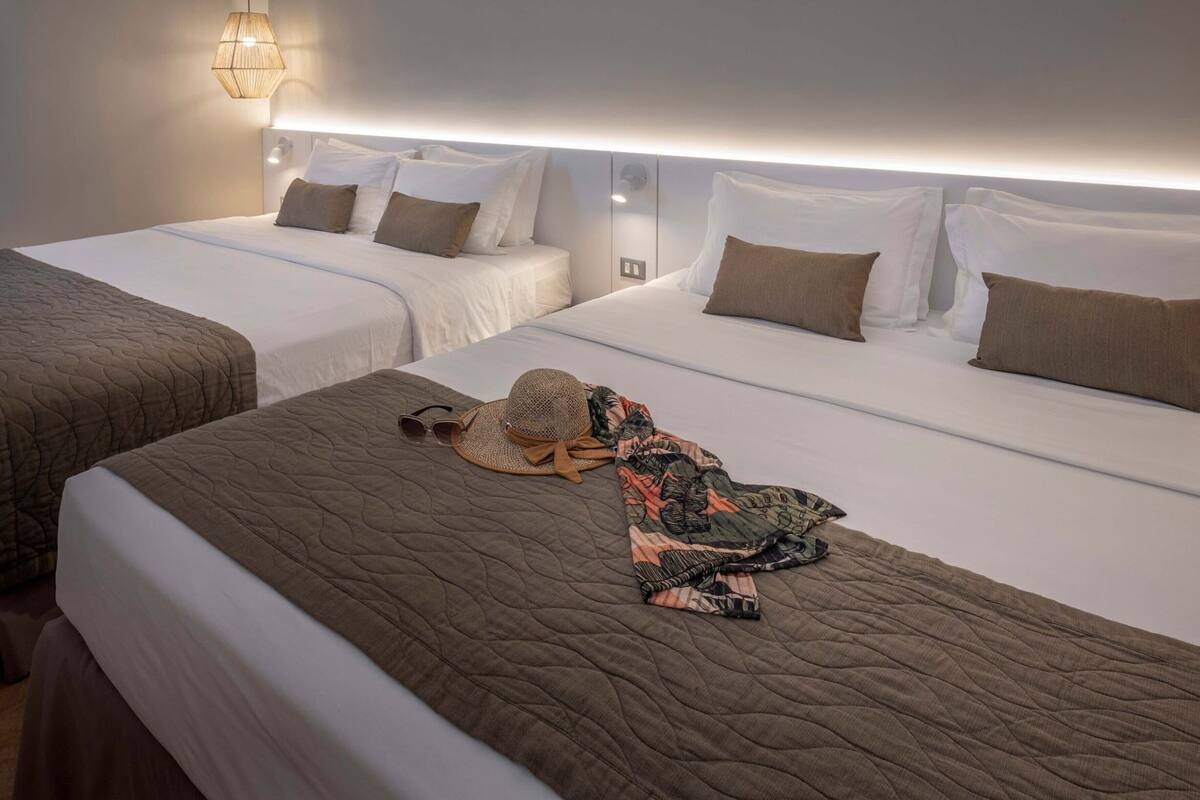 A hotel room with two beds, a large mirror, and a wall-mounted light fixture.